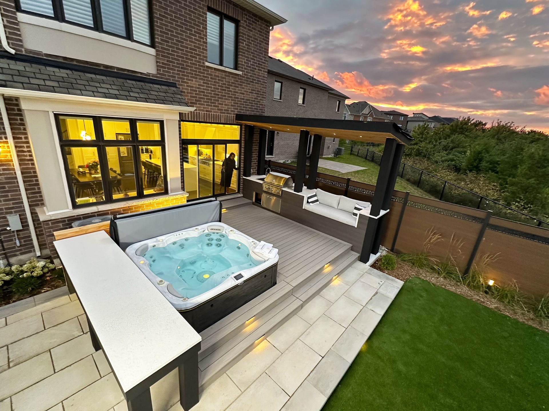 Hydropool hot tub on a backyard patio at dusk with pergola and outdoor kitchen