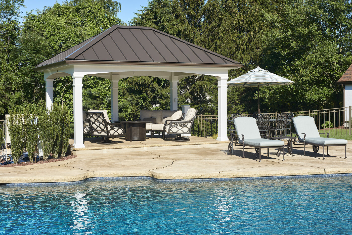 Custom pavilion with metal roof and stone fireplace beside a backyard pool